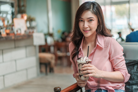 young woman holding chocolate frappe with whipped cream in the cafeの写真素材