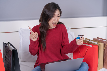surprised woman using laptop for online shopping with credit card on a bed
