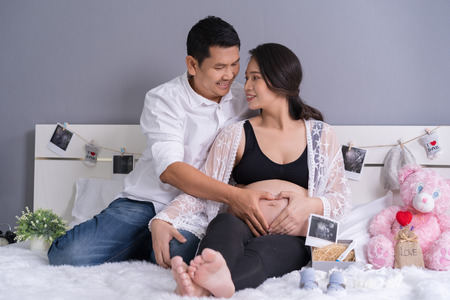 husband and his pregnant wife showing heart with hands in the bedの写真素材