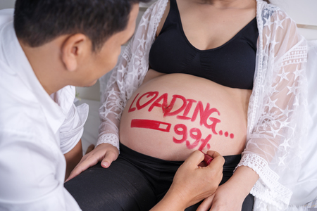 husband writting word "loading 99%" on belly of his pregnant wifeの写真素材