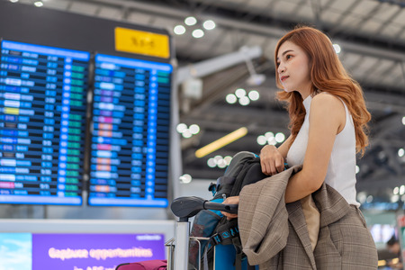 beautiful woman waiting for flight with information board in airportの写真素材