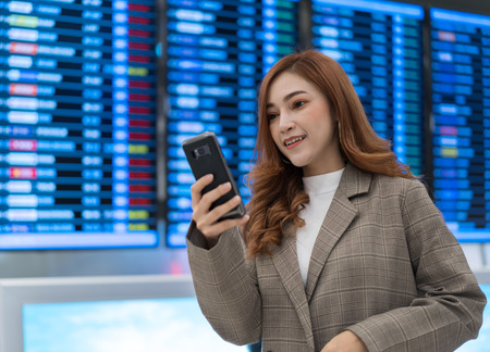 beautiful woman using smartphone with flight information board at airportの写真素材