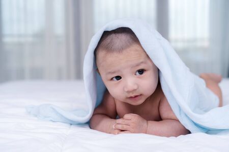 happy baby lying on bed under blanket in a bedroom
