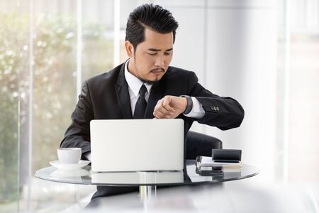 young business man checking time on smart watch while using laptopの写真素材