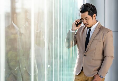 depressed young business man is talking on smartphone in officeの写真素材