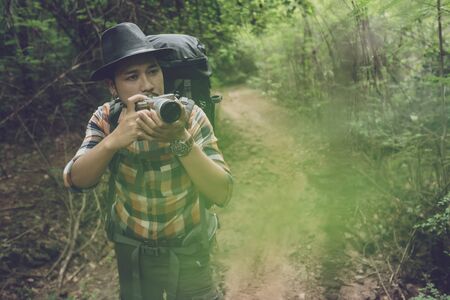 man traveler with backpack using camera to take a photo in the natural forestの写真素材