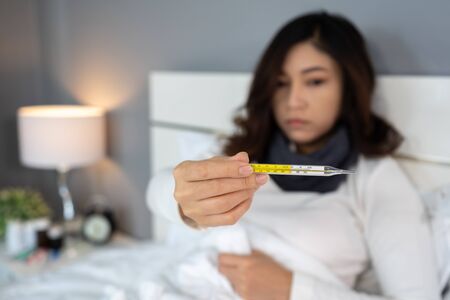 sick woman using thermometer and showing high temperature in bedの写真素材