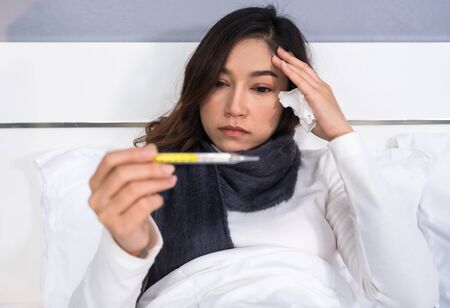 sick woman using thermometer to checking her temperature and her headache in a bedの写真素材