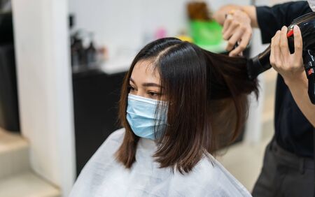 hairdresser using hair dryer and comb to the hair of woman, people must be wering a medical mask to protection coronavirus (covid-19) pandemic. new normal conceptsの写真素材