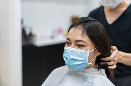 hairdresser cutting the hair to a female client, people must be wering medical mask to protection...