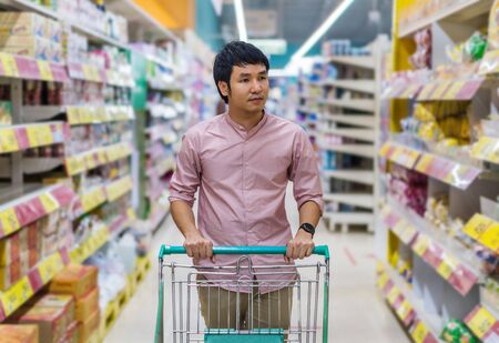 young asian man with shopping cart in supermarket department storeの写真素材