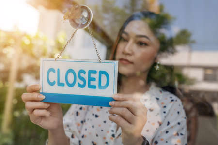 young woman owner turning closed sign in door of store