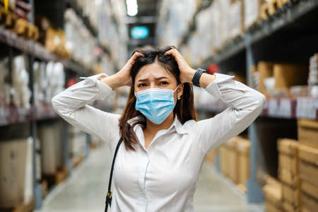 stressed woman with medical mask in the warehouse store during coronavirus (covid-19) pandemic.の写真素材
