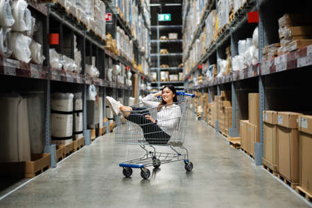 young cheerful woman sitting in shopping cart at warehouse store