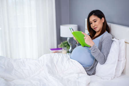 pregnant woman reading a book on a bedの写真素材