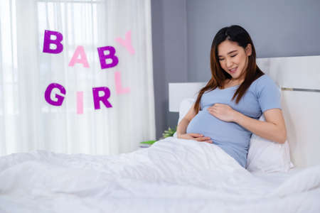 pregnant woman stroking her belly on a bed with baby girl signの写真素材