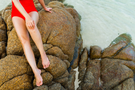Close up of a legs of woman in swimsuit sitting on stone rock at the sea beachの写真素材