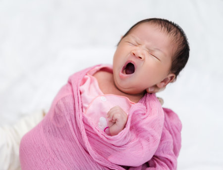 mother holding sleepy newborn baby yawning in her armの写真素材