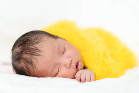 newborn baby sleeping in yellow fur blanket on a bedの写真素材