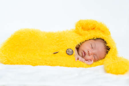 newborn baby in bunny fur suit sleeping on a bedの写真素材