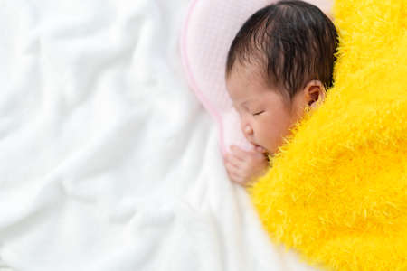 newborn baby sleeping in yellow fur blanket on a bedの写真素材