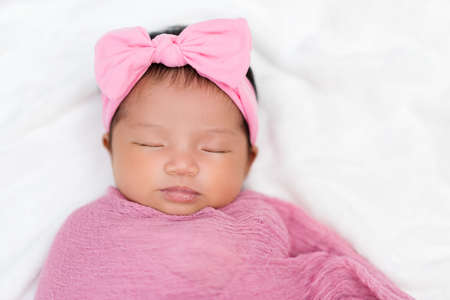 newborn baby sleep in pink cloth wrap blanket on a bed
