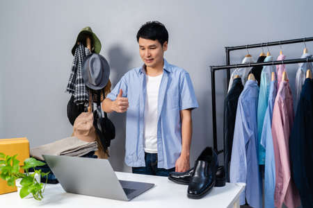 young man selling clothes and accessories online by laptop computer live streaming, business online e-commerce at homeの写真素材