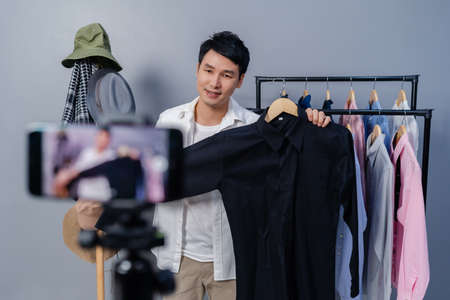 young man selling clothes and accessories online by smartphone live streaming, business online e-commerce at homeの写真素材