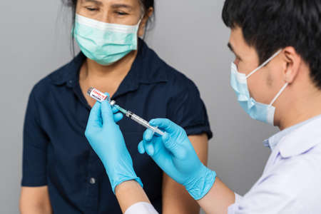 doctor draws medication out of vial before injection with syringe to woman and wearing a medical mask.の写真素材
