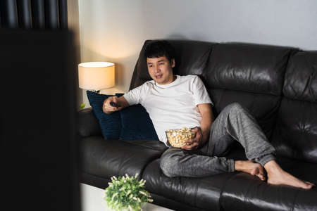 happy young man watching TV on sofa at nightの写真素材