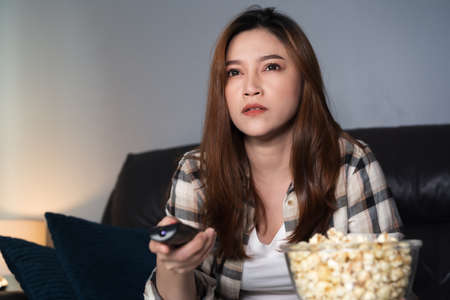 young woman watching TV on sofa at nightの写真素材
