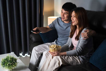 happy young couple watching TV on sofa at night