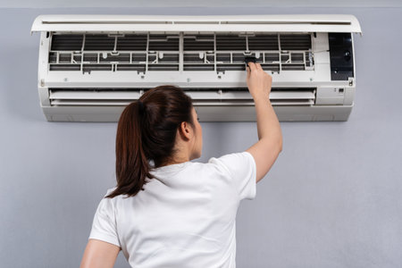 young woman using brush to cleaning the air conditioner indoors at honeの写真素材
