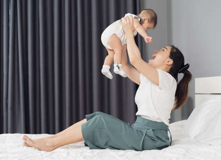 mother holding baby newborn in her arms lifting up on a bed at homeの写真素材