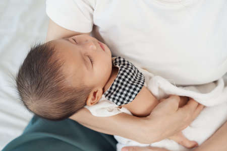 mother holding newborn baby sleeping in her arm on a bedの写真素材