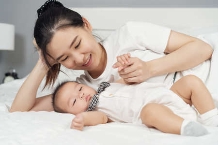 happy mother and baby lying on a bed at homeの写真素材