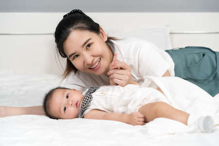 happy mother and baby lying on a bed at homeの写真素材