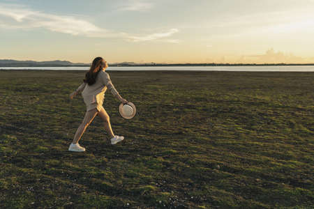 cheerful woman walk across the green field with sunsetの写真素材