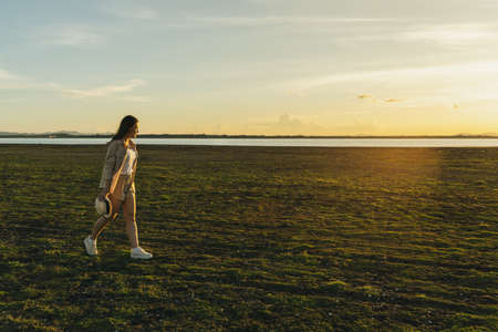 cheerful woman walk across the green field with sunset