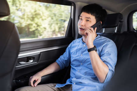young man talking on mobile phone while sitting in the back seat of car