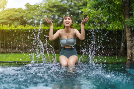 young woman sitting on edge of swimming pool and playing water splashingの写真素材