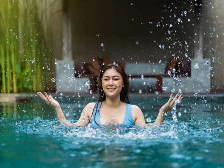 cheerful young woman playing water splashing in the swimming pool