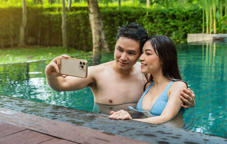 happy young couple taking selfie photo at edge of swimming poolの写真素材
