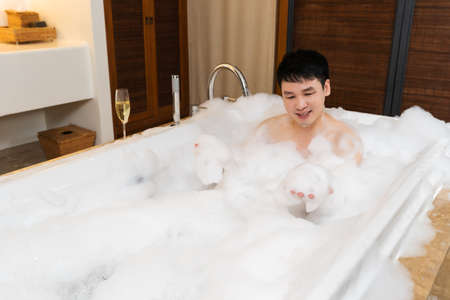 young man washing body and playing bubble foam in bathtubの写真素材