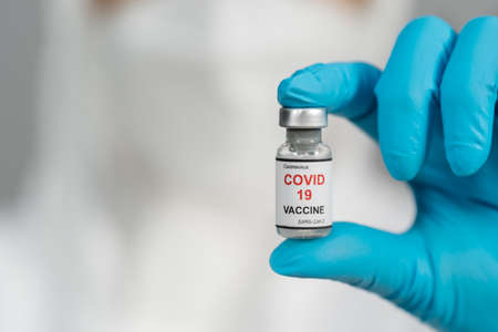 doctor in protective PPE suit holding Coronavirus (Covid-19) vaccine bottle