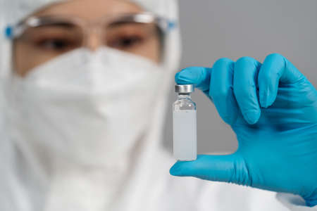 doctor in protective PPE suit holding and gently shaking vaccine bottle