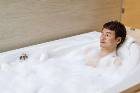 young man relaxing in bathtube with eyes closed in bathroomの写真素材