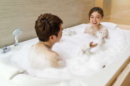 young couple washing body and playing with bubble foam in bathtub