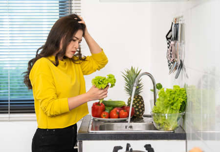 stressed young woman washing vegetables in the sink in the kitchen at homeの写真素材