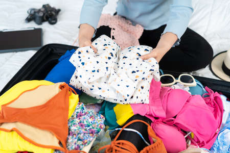 young woman preparing and packing clothes into suitcase on a bed at home, holiday travel concept